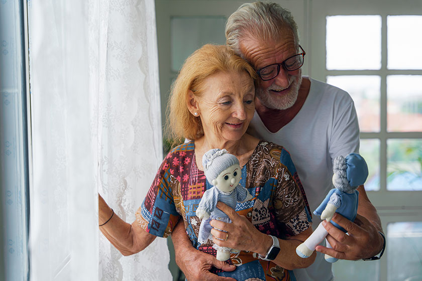 caucasian senior husband wife couple standing windowat home old dolls