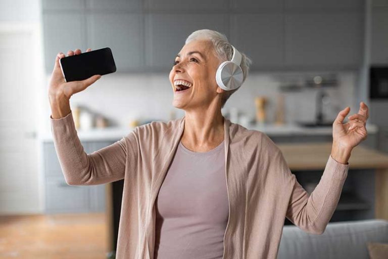 Cheerful european senior lady smartphone headphones singing song having fun