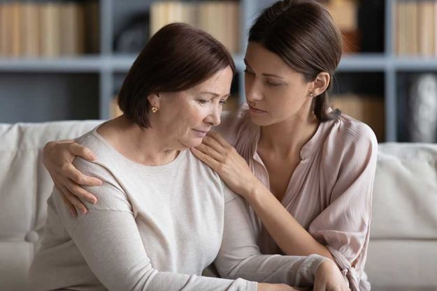 Compassionate woman embracing shoulder of unhappy stressed middle aged mommy