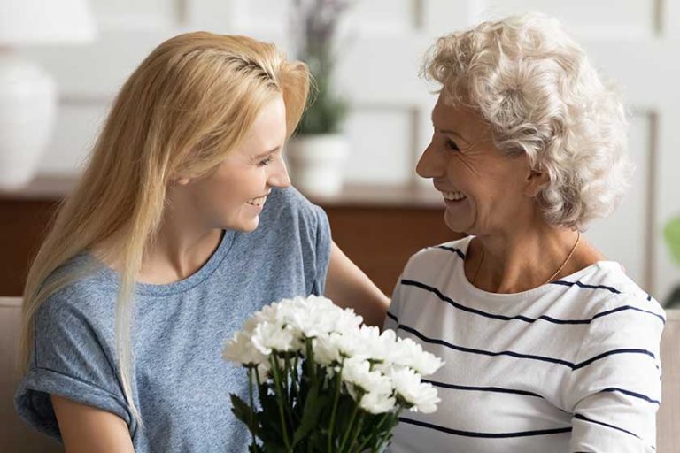 Young smiling blonde grown up daughter congratulating happy mother Young smiling blonde grown up daughter congratulating happy mother