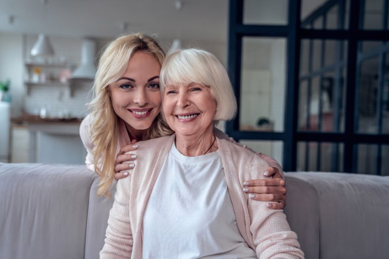 Senior woman and her attractive daughter spending time together at home and sitting on sofa. Happy Mothers’ Day. Senior woman and her attractive daughter spending time together at home and sitting on sofa. Happy Mothers' Day.