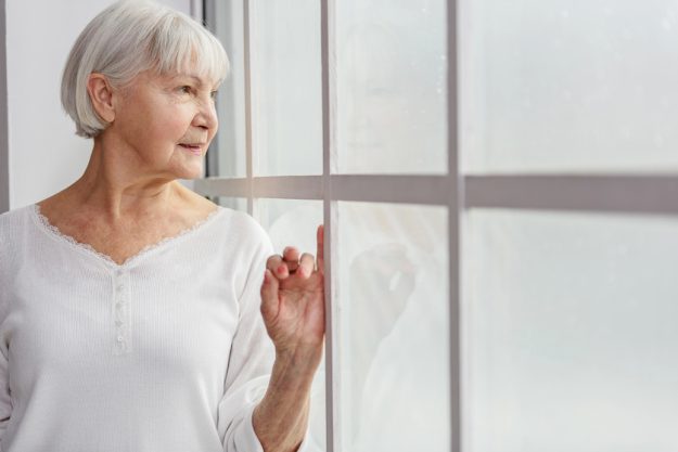 Cheerful pensioner watching at closed window in hospital — Photo