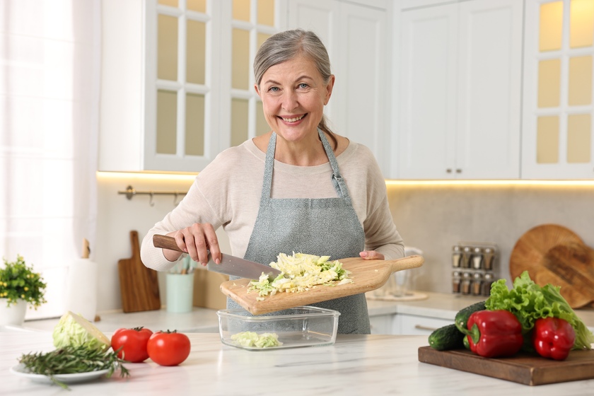 Happy housewife putting cut cabbage into glass container at white marble table in kitchen — Photo