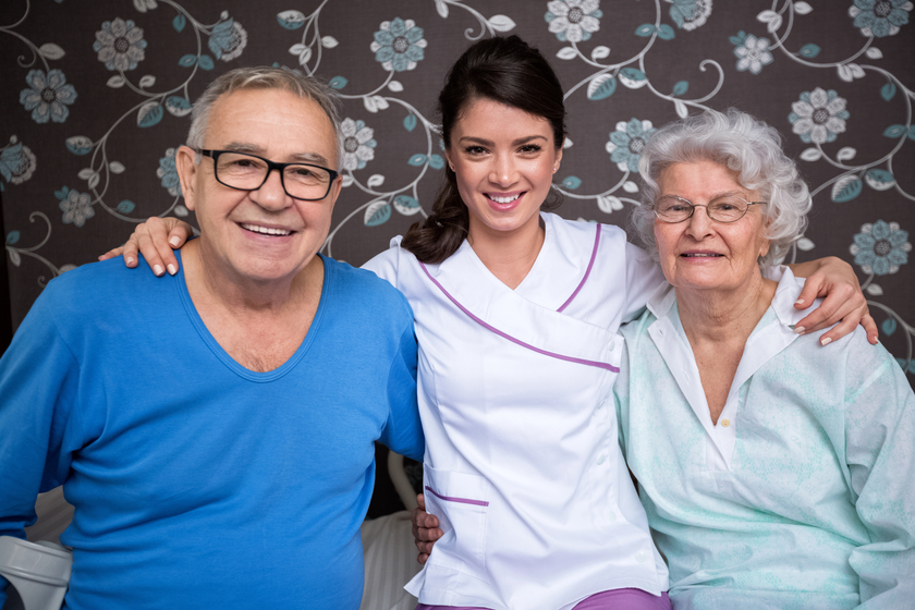 Smiling satisfied elderly people with nurse at nursing home