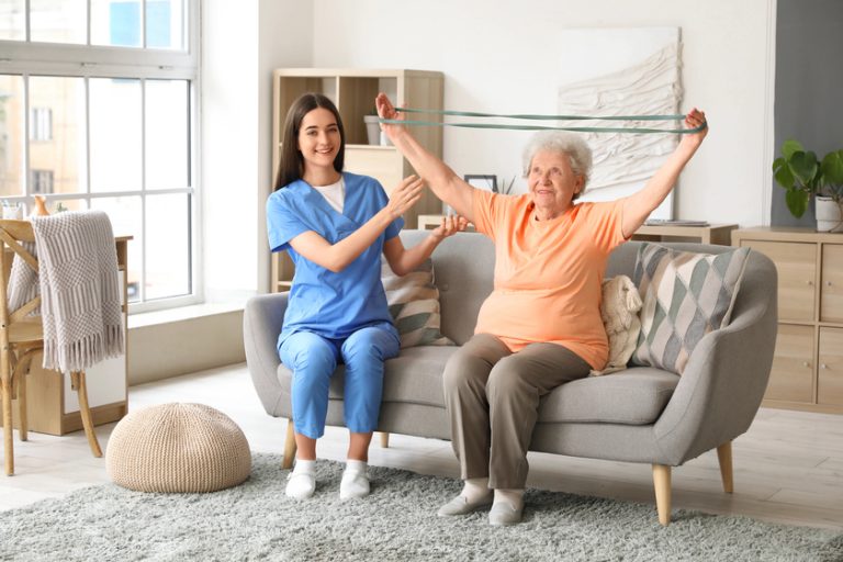 Young nurse and senior woman with stretching band training at home