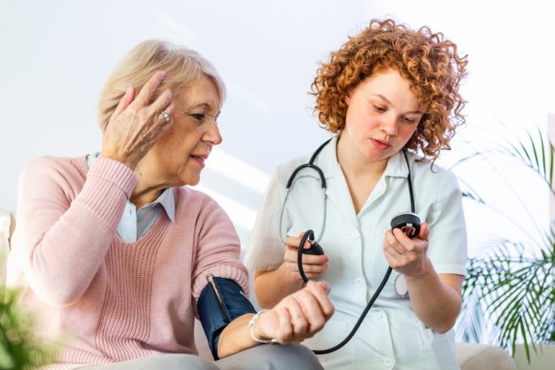 Young nurse measuring blood pressure of elderly woman at home. Female nurse checking blood pressure of a senior woman at home,Home carer checking patients blood pressure