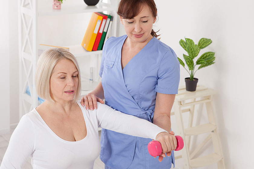A physiotherapist helps an older woman recover from an injury through exercise with dumbbells A physiotherapist helps an older woman recover from an injury through exercise with dumbbells