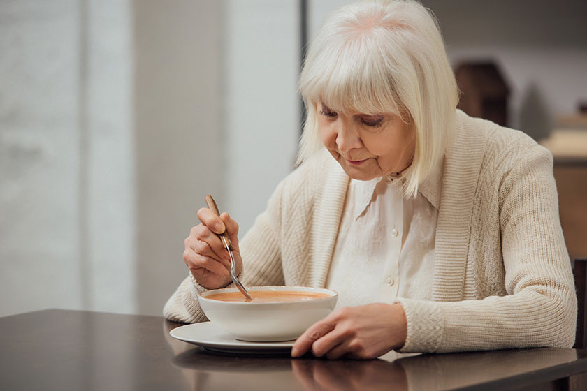 Senior woman grey hair sitting table eating cream soup home Senior woman grey hair sitting table eating cream soup home