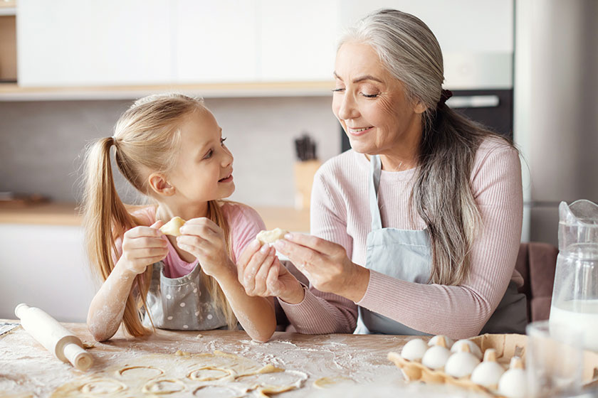 Smiling old grandmother apron teaching little granddaughter making dough mold