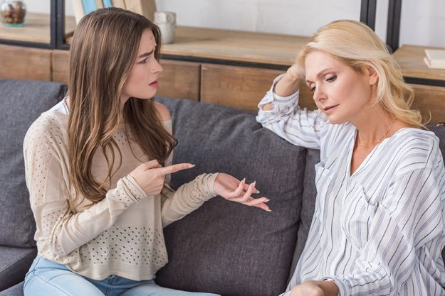 Dissatisfied girl pointing finger upset mother while sitting sofa together