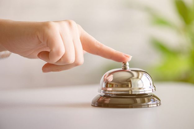 Hand guest ringing silver bell reception desk copy space hotel