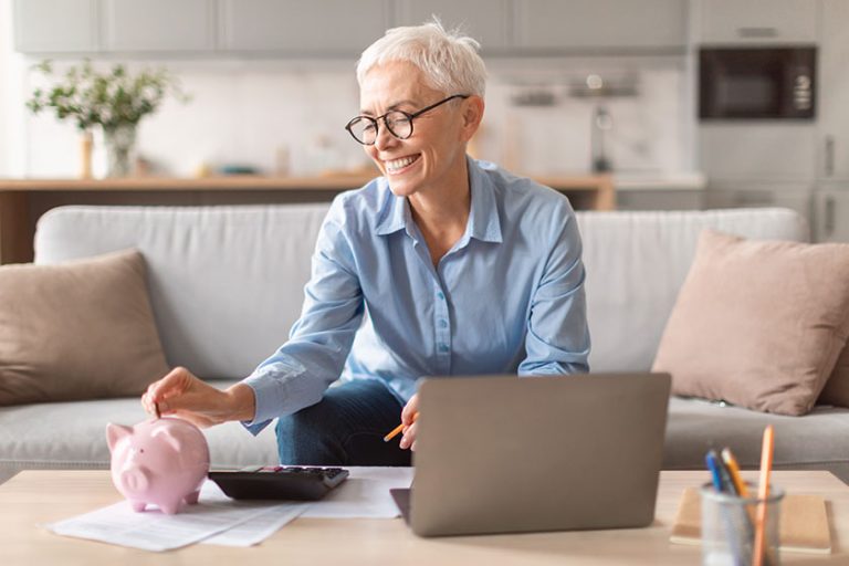 Happy european mature woman holding putting money coin pink piggybank Happy european mature woman holding putting money coin pink piggybank
