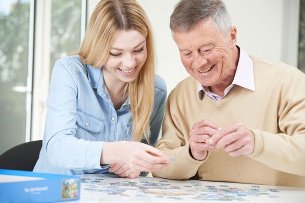 Teenage granddaughter helping grandfather with jigsaw puzzle