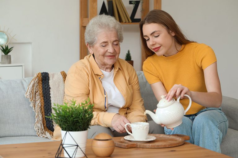 Young woman pouring tea cup her grandmother home