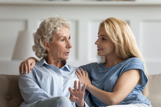 Mature mom and adult daughter relax talking at home