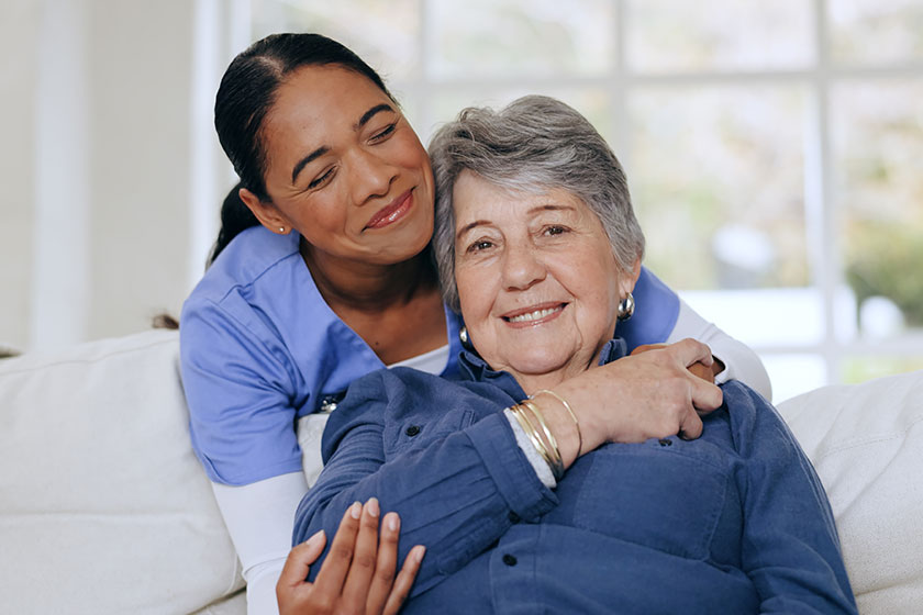Senior woman nurse hug sofa retirement home caregiver support smiling