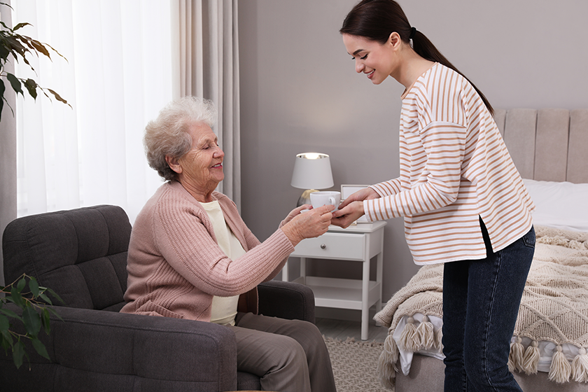 young caregiver giving tea senior woman