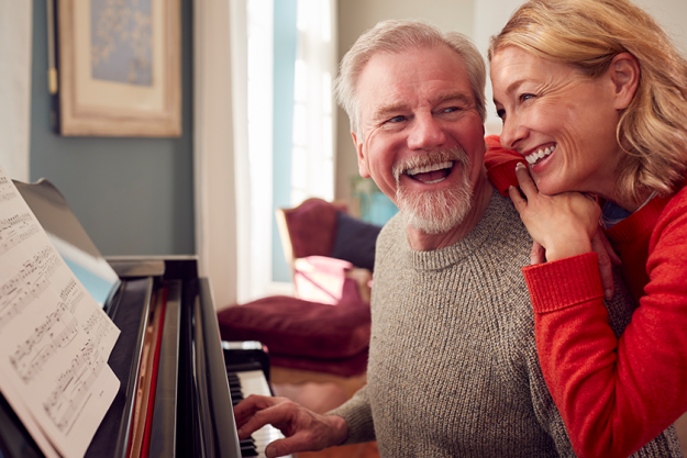 Smiling senior couple home enjoying learning play piano