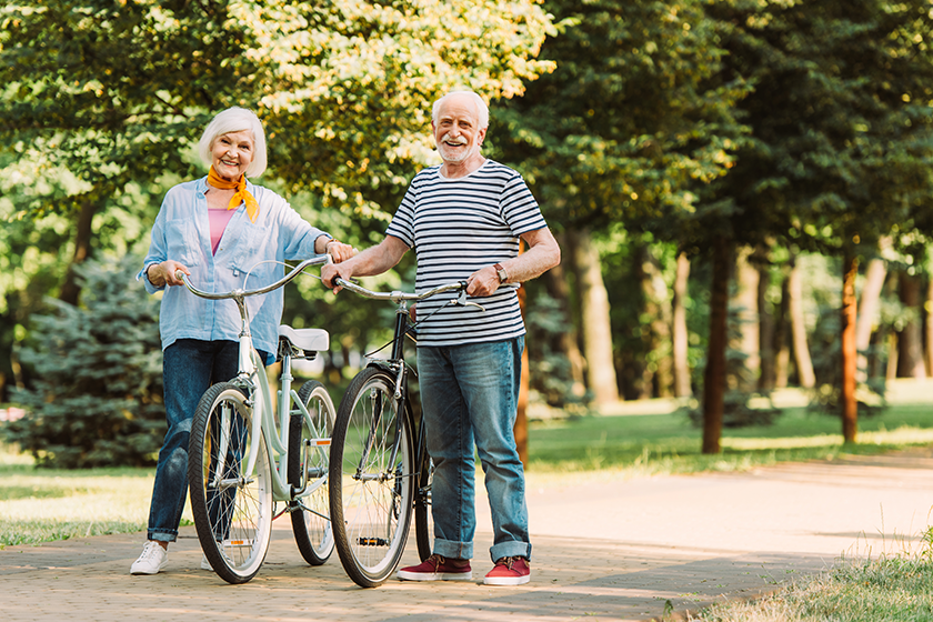 elderly couple smiling camera while walking bicycles
