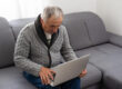 Older man sitting on sofa, smiling at computer screen at home