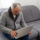 Older man sitting on sofa, smiling at computer screen at home