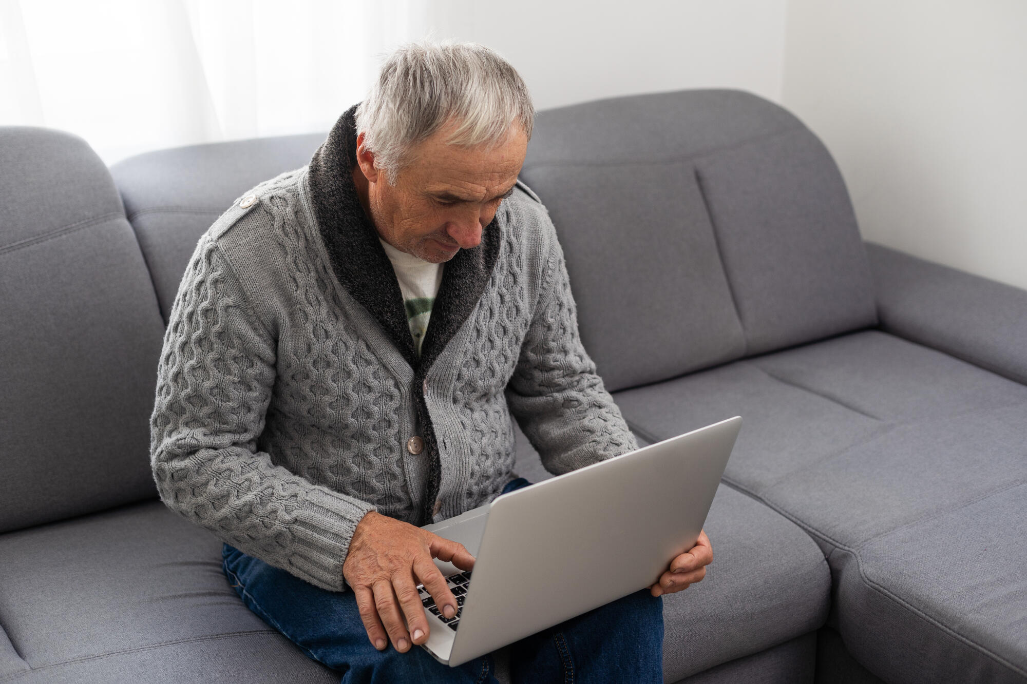 Older man sitting on sofa, smiling at computer screen at home